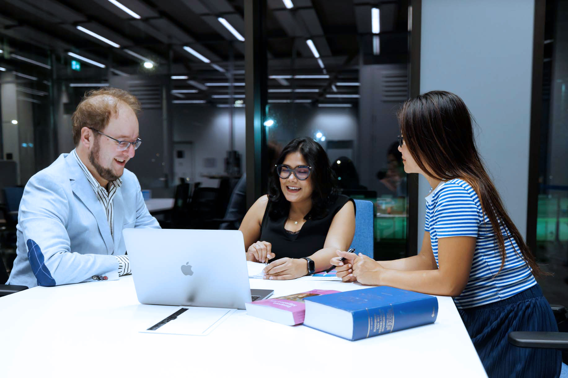 A group of people sitting around a table in front of a laptop discussing employer-employee relations.